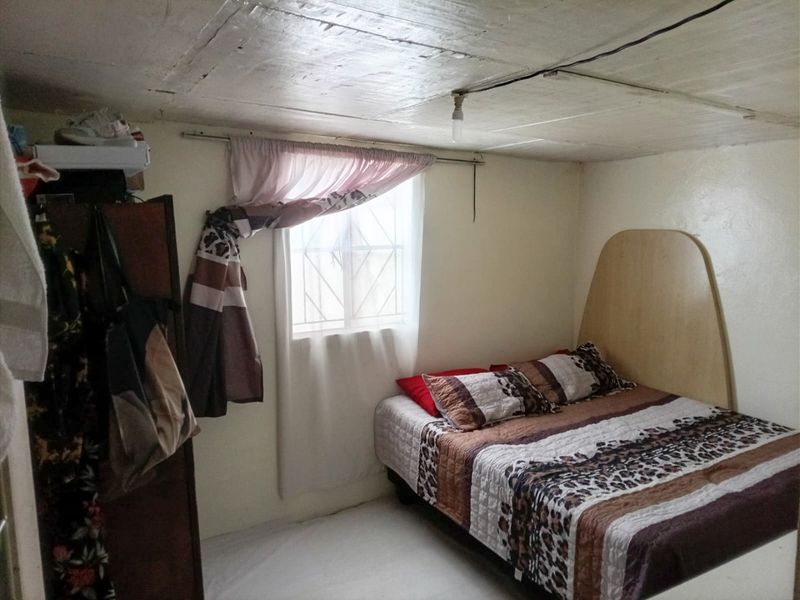 A compact bedroom featuring a window with security bars and a basic ceiling finish with exposed wiring.