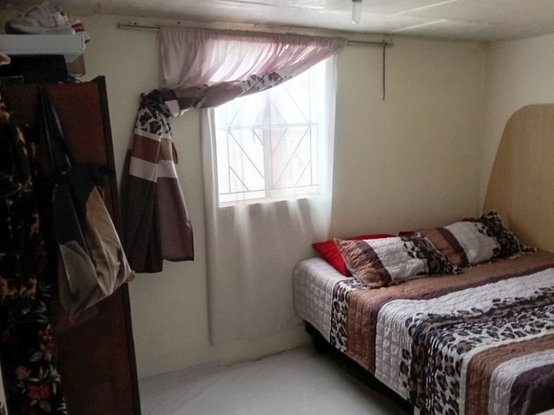 A compact bedroom featuring a window with security bars and basic ceiling finishes, requiring cosmetic updates to improve the overall aesthetic.