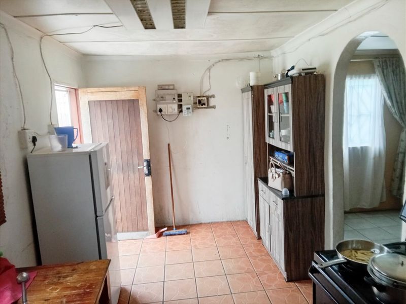 A functional kitchen area featuring tiled flooring, an arched entryway, and exposed electrical infrastructure, offering potential for modernization and cosmetic updates.