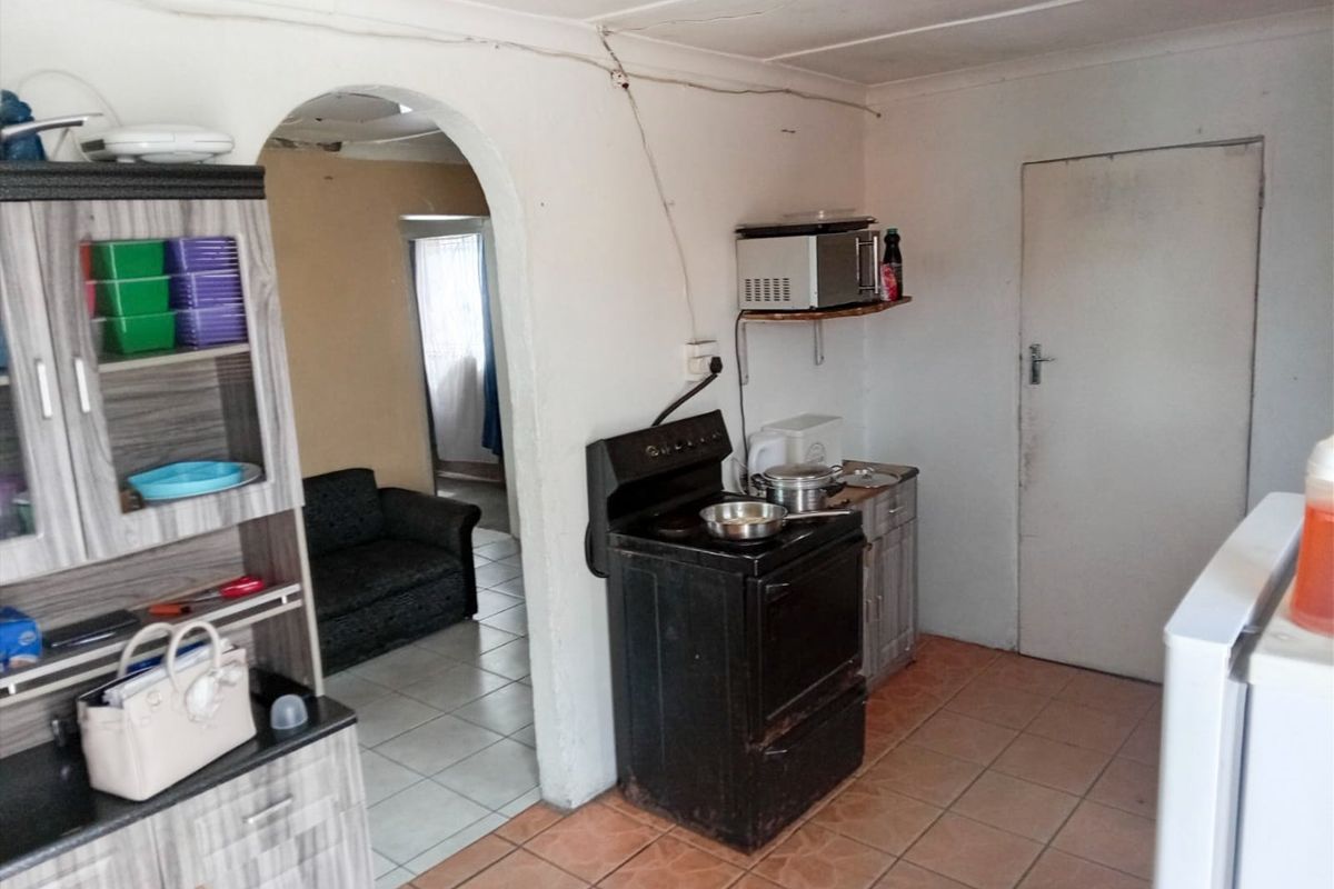 A functional kitchen area featuring tiled flooring, an arched entryway, and a freestanding stove, requiring cosmetic updates to improve its overall condition.
