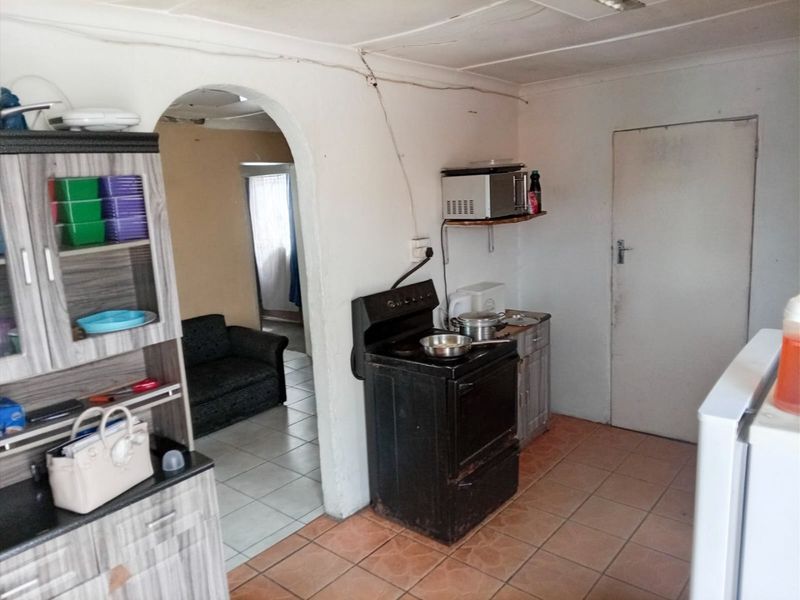 A functional kitchen area featuring tiled flooring, an arched entryway, and a freestanding stove, requiring cosmetic updates to improve its overall condition.