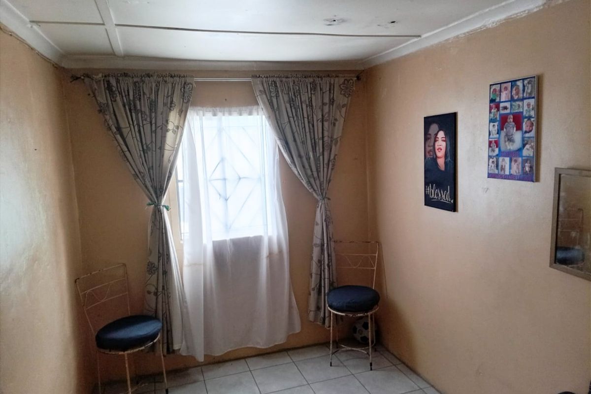 A bedroom featuring tiled flooring and a window with security bars. The room requires cosmetic updates to the walls and ceiling.