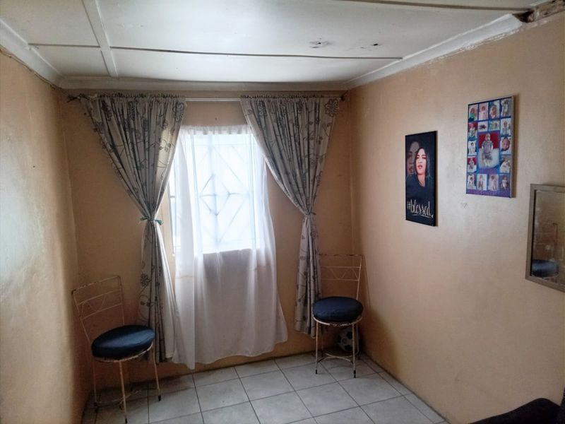 A bedroom featuring tiled flooring and a window with security bars. The room requires cosmetic updates to the walls and ceiling.
