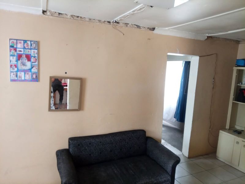 A living area featuring tiled flooring and a built-in shelving unit, currently requiring significant maintenance and repair to the ceiling and wall finishes.