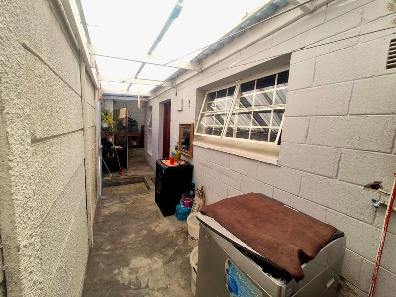 A functional outdoor laundry area featuring concrete flooring, a translucent roof covering, and security-barred windows, providing a practical utility space.