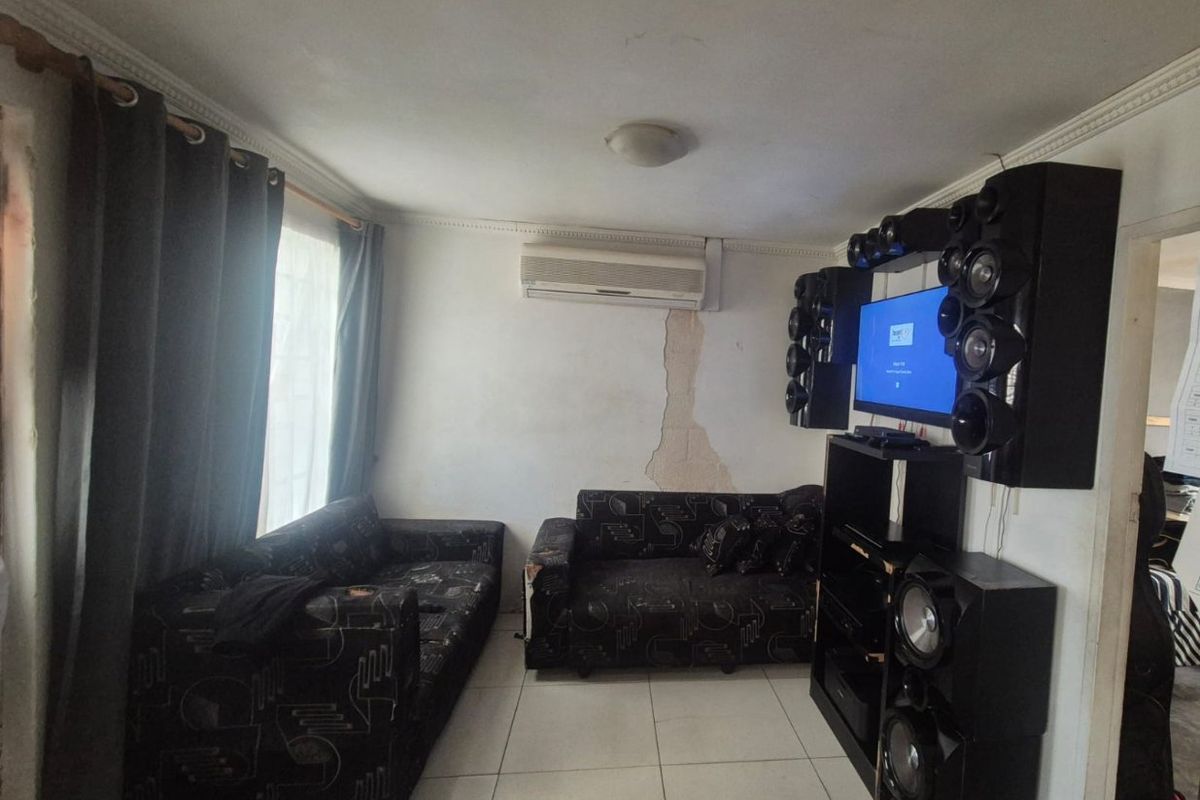 A living room featuring tiled flooring, cornicing, and a wall-mounted air conditioning unit, currently showing visible damage to the wall plaster.