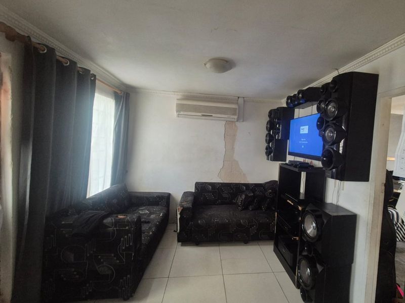 A living room featuring tiled flooring, cornicing, and a wall-mounted air conditioning unit, currently showing visible damage to the wall plaster.