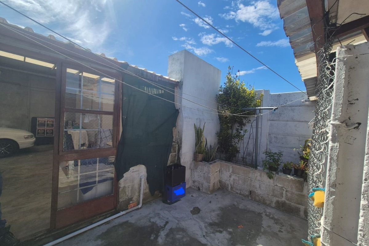 A rear courtyard area featuring a concrete patio, masonry boundary walls, and a timber-framed glass door leading into the property.