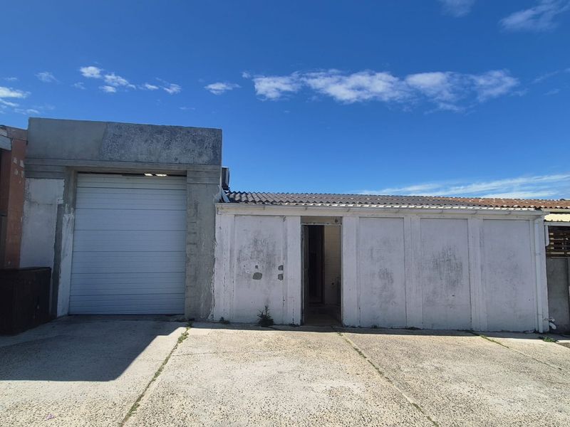 A detached garage structure featuring a roller shutter door and a concrete driveway, showing significant signs of exterior wear and weathering.