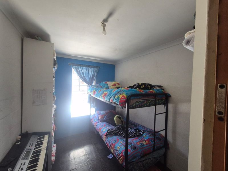 A compact bedroom featuring built-in shelving and a window, currently utilized as a children's room with basic finishes.