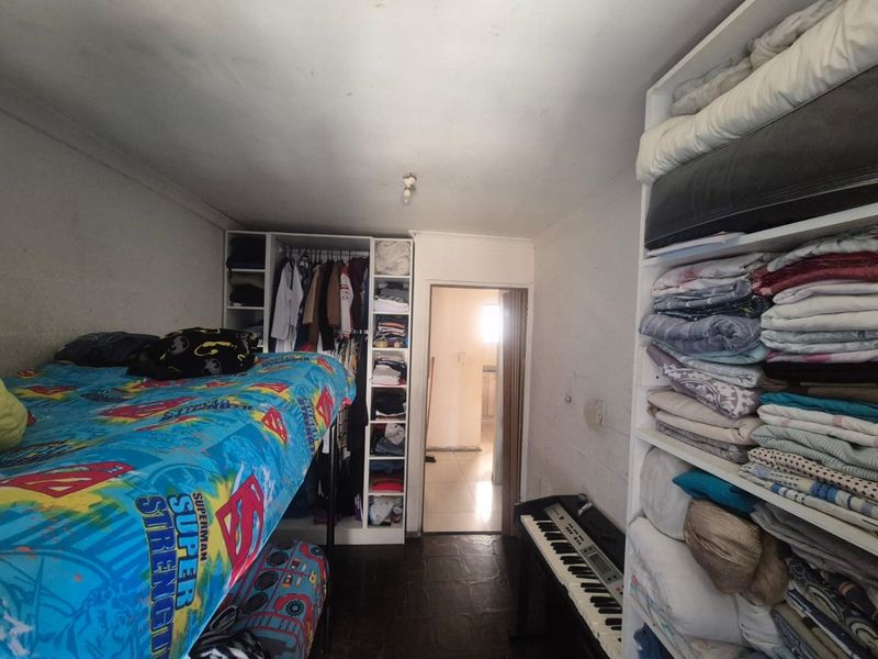 A compact bedroom featuring built-in wardrobe storage and shelving units, with tiled flooring and direct access to an adjacent room.