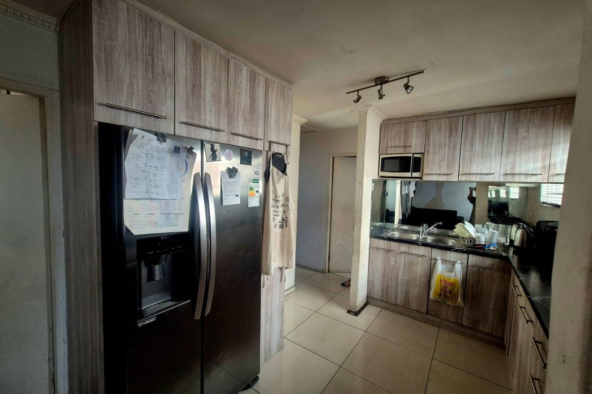 A functional kitchen featuring wood-look cabinetry, a double sink, built-in microwave, and tiled flooring, offering a practical layout for daily meal preparation.