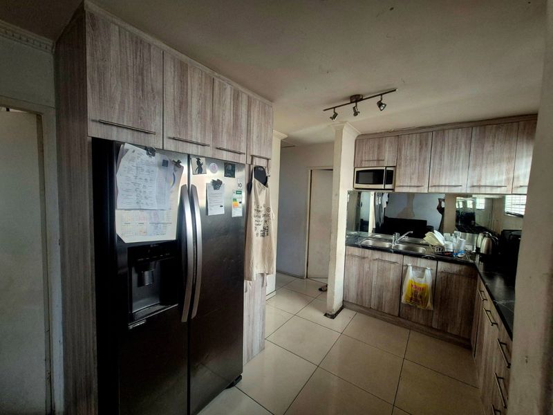 A functional kitchen featuring wood-look cabinetry, a double sink, built-in microwave, and tiled flooring, offering a practical layout for daily meal preparation.