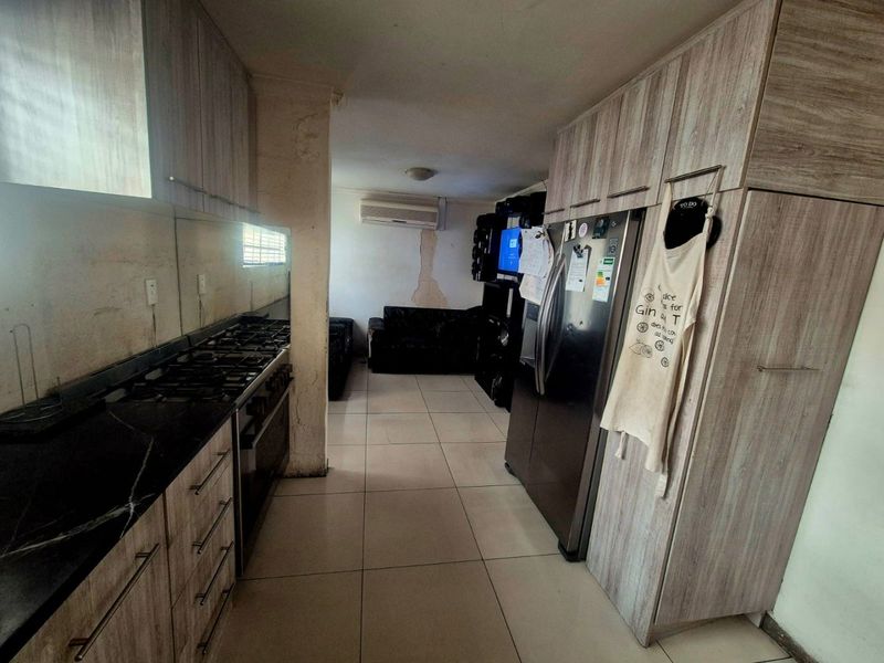 Open-plan kitchen and living area featuring built-in cabinetry, gas hob, and tiled flooring, currently showing signs of wall damage and wear.