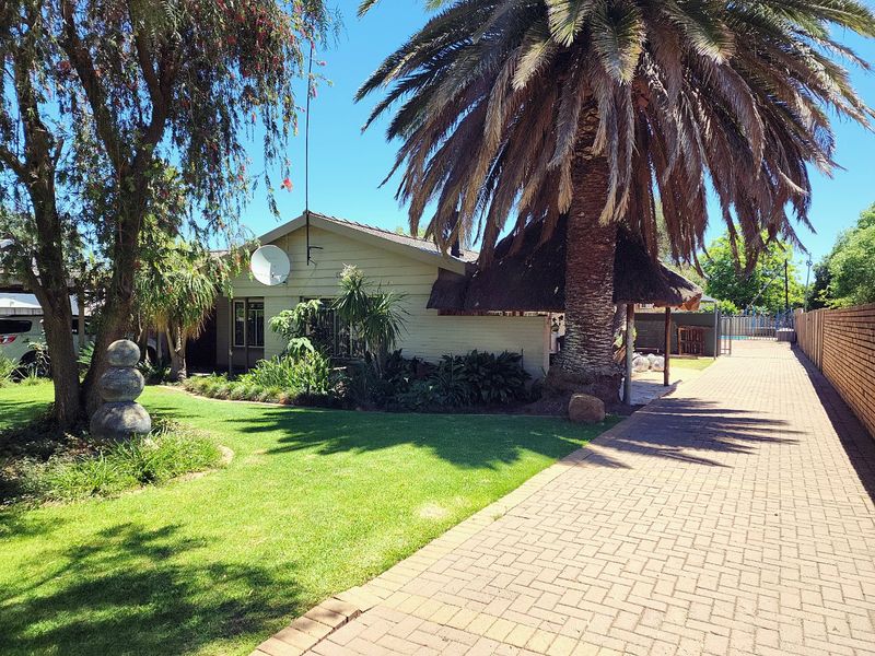 Front exterior view featuring a paved driveway, landscaped garden, and a covered thatched outdoor area adjacent to the main house structure.