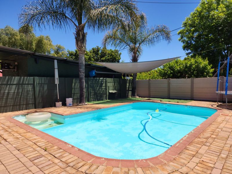 Outdoor pool area featuring a swimming pool with brick paving surround, shade sail, and perimeter fencing.