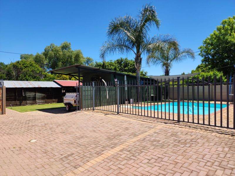 Outdoor area featuring a swimming pool, paved driveway, metal fencing, and a covered patio structure with an adjacent timber shed.
