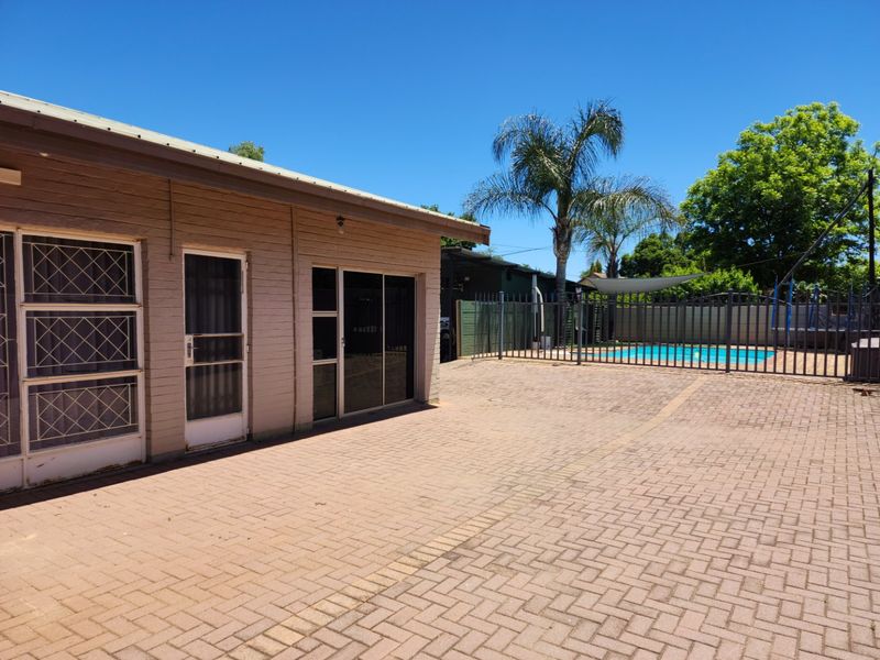 Rear exterior view featuring a paved patio area, sliding glass doors, and a fenced swimming pool in the background.