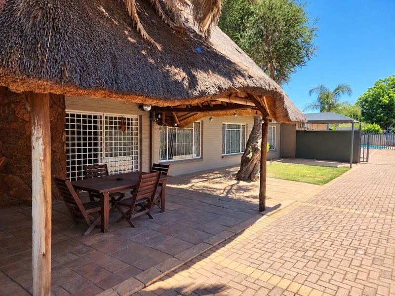 Covered patio area featuring a traditional thatched roof, brick paving, and direct access to the garden through security-gated sliding doors.