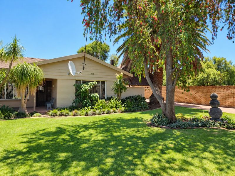 Front view of a well-maintained single-story house featuring a brick facade, tiled roof, satellite dish, and a landscaped garden with a paved driveway.