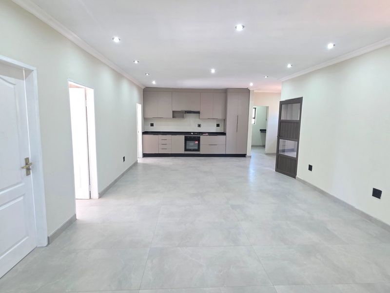 Spacious open-plan living area featuring modern neutral cabinetry, integrated kitchen appliances, large format floor tiles, and recessed ceiling lighting.