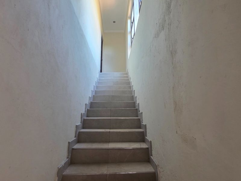 A vacant interior staircase featuring tiled steps and large windows, currently showing significant wall surface wear and staining requiring maintenance.