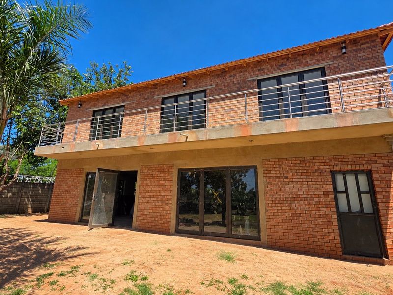 Rear view of a double-storey face brick apartment building featuring a large balcony with stainless steel balustrades and aluminium sliding doors.