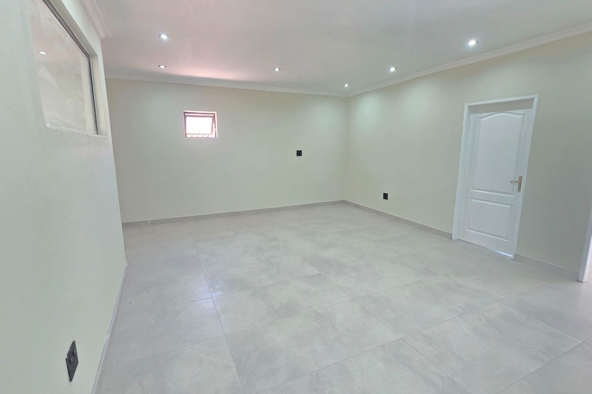 A bright, empty living area featuring neutral tiled flooring, recessed downlighting, and clean white walls, providing a versatile blank canvas for interior design.