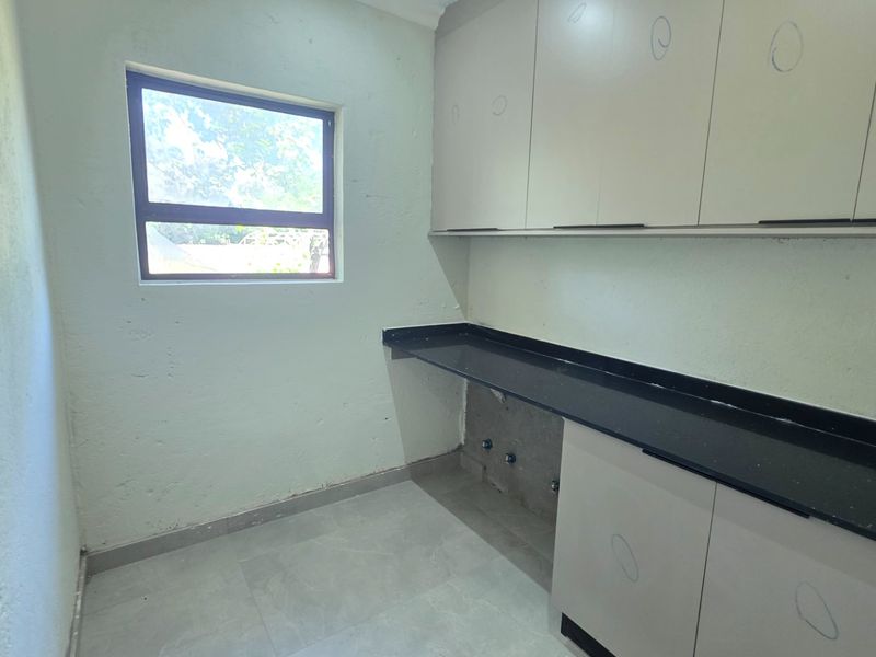 A functional scullery area featuring built-in cabinetry, a dark granite countertop, and plumbing connections, providing a clean and practical utility space.