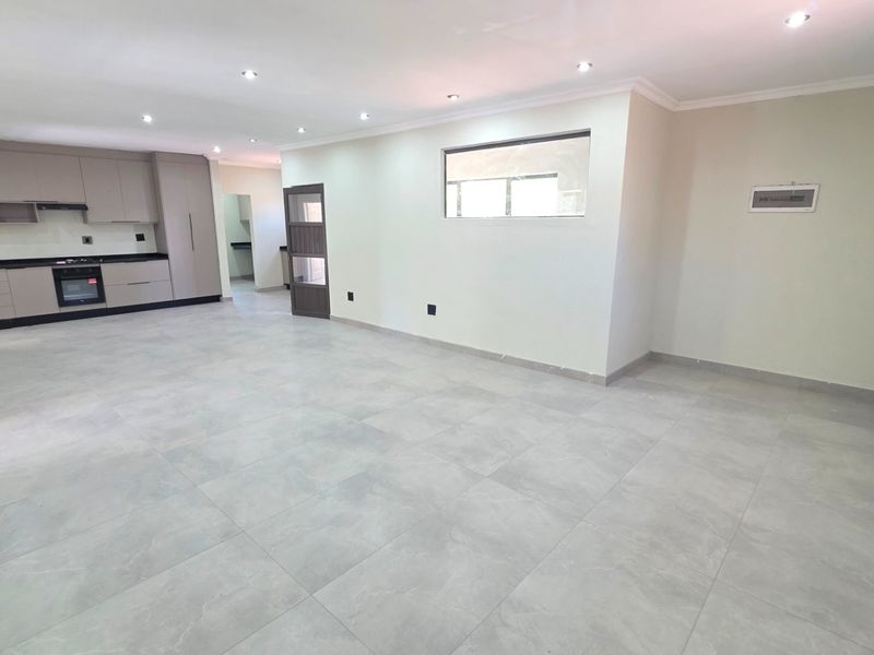 Spacious open-plan living area featuring modern tiled flooring, recessed lighting, and a sleek, contemporary kitchen with integrated appliances.