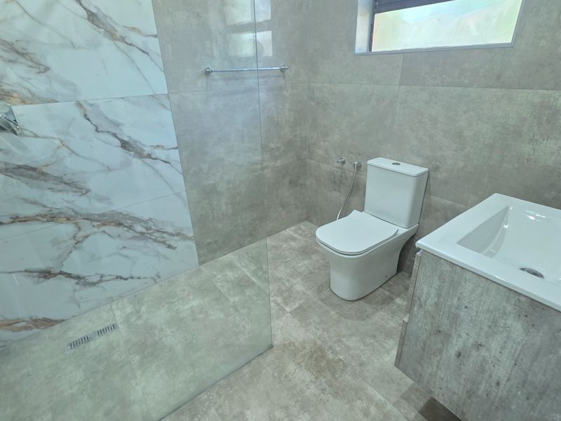 Modern bathroom featuring a walk-in shower with marble-effect tiling, a sleek vanity unit, and contemporary grey floor-to-ceiling wall tiles.