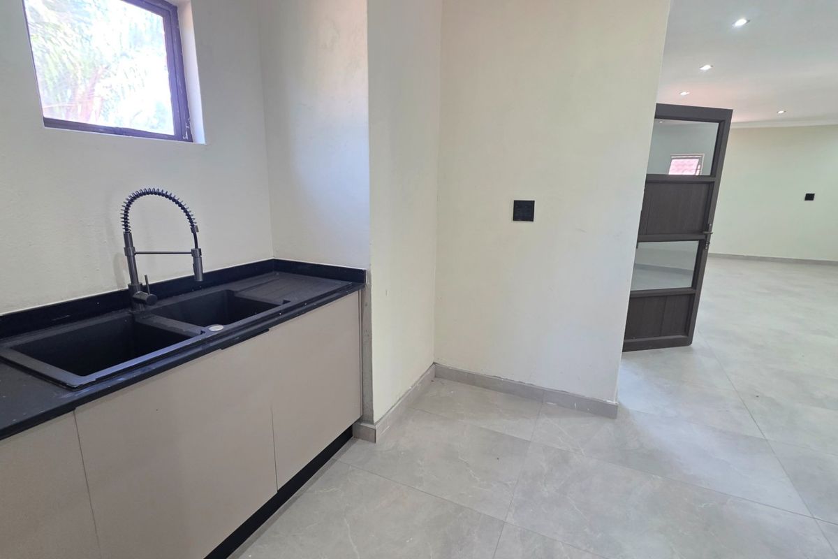 A modern, minimalist kitchen area featuring sleek cabinetry, a dark stone countertop with a double basin sink, and neutral tiled flooring.