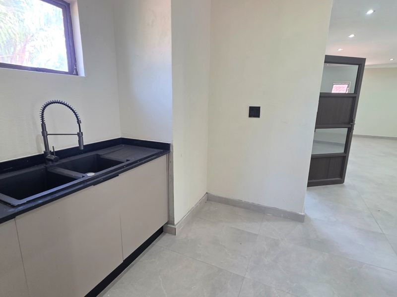 A modern, minimalist kitchen area featuring sleek cabinetry, a dark stone countertop with a double basin sink, and neutral tiled flooring.
