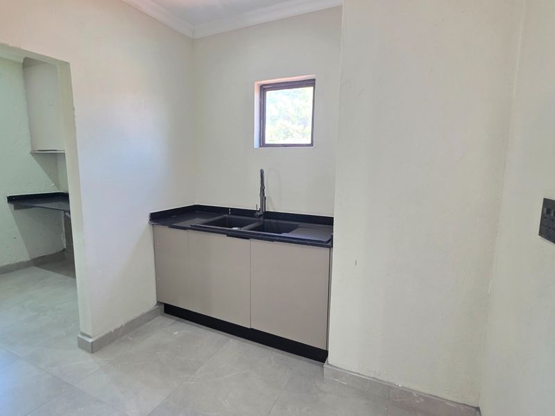 A clean, empty scullery area featuring modern built-in cabinetry, a dark stone countertop with a double sink, and neutral tiled flooring.