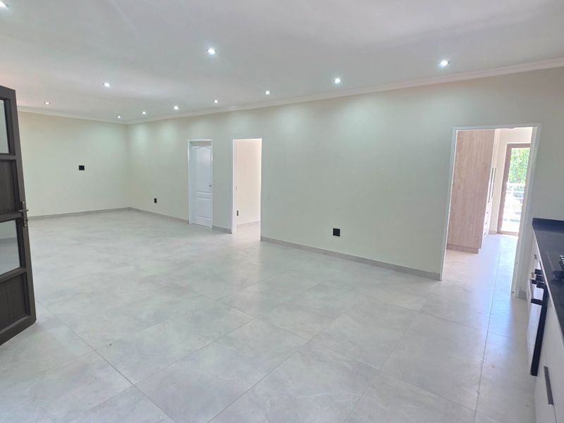 Spacious open-plan living area featuring modern tiled flooring, recessed downlights, and a sleek kitchen with stone countertops and built-in cabinetry.