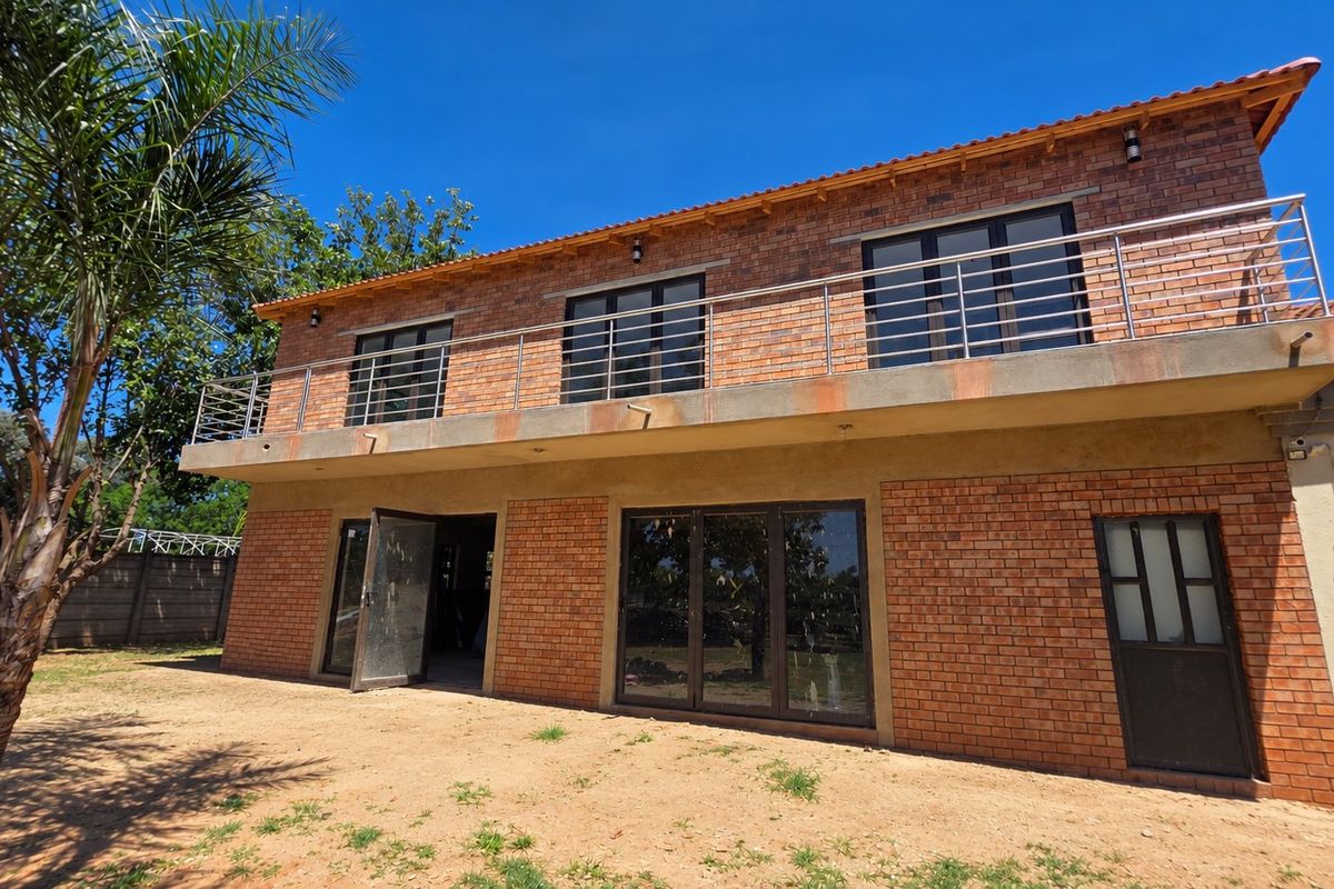 Rear view of a double-story face brick apartment building featuring a large balcony with stainless steel balustrades and aluminium sliding doors.