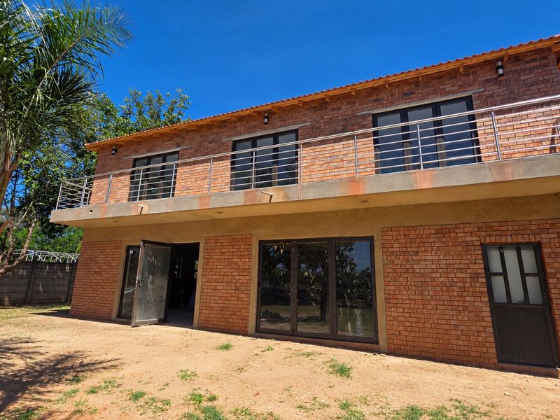 Rear view of a double-story face brick apartment building featuring a large balcony with stainless steel balustrades and aluminium sliding doors.