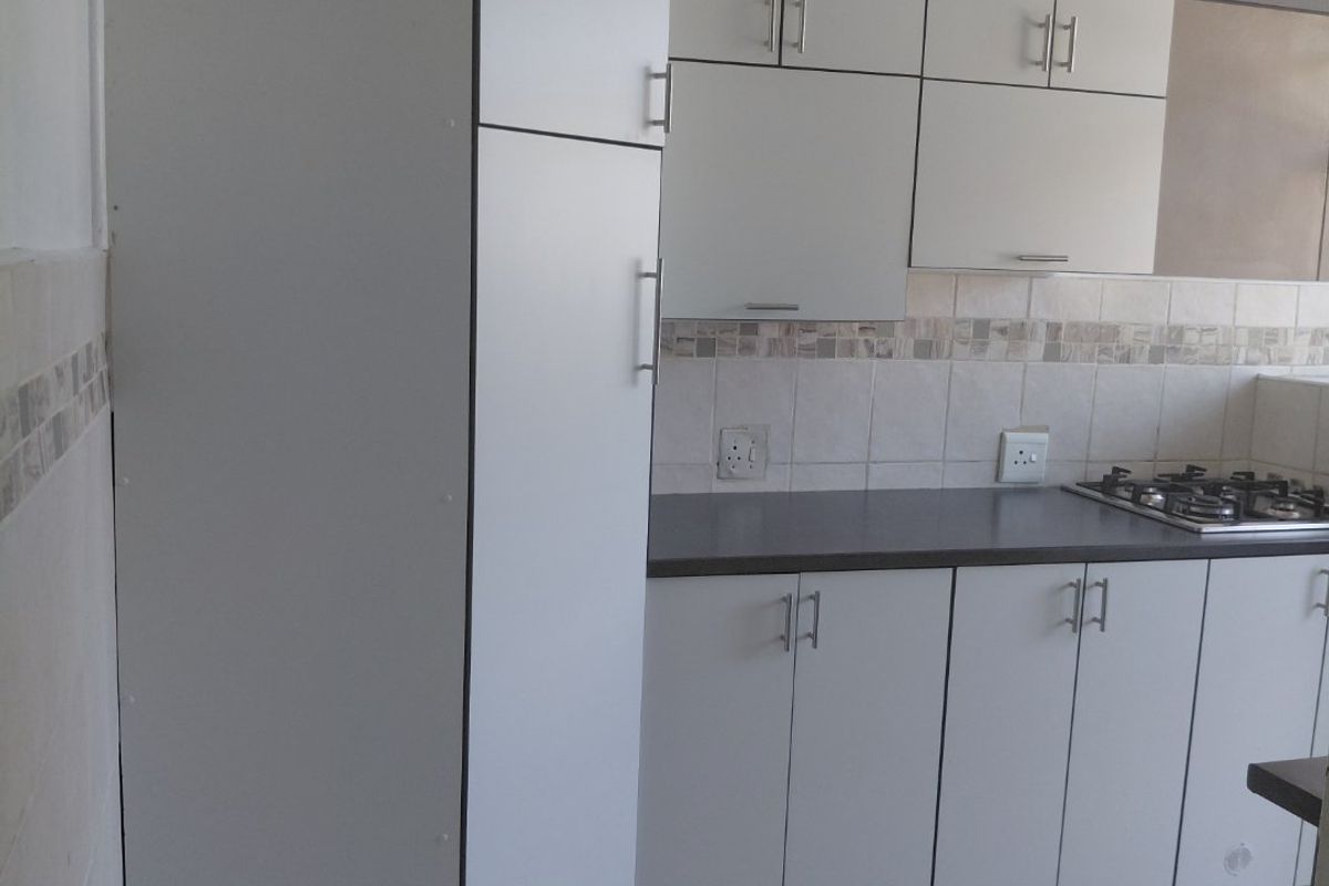 A clean, functional kitchen featuring white built-in cabinetry, a dark laminate countertop, a gas hob, and neutral tiled flooring and backsplash.