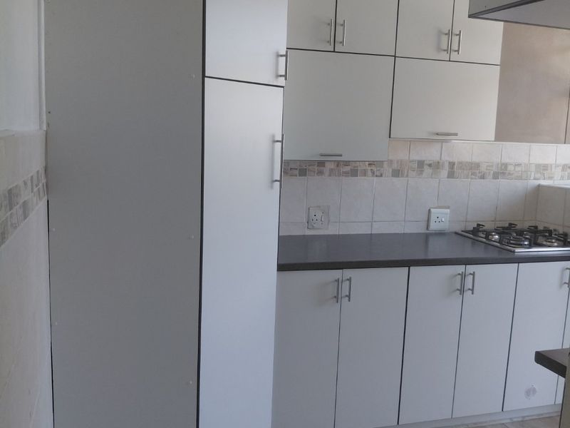 A clean, functional kitchen featuring white built-in cabinetry, a dark laminate countertop, a gas hob, and neutral tiled flooring and backsplash.