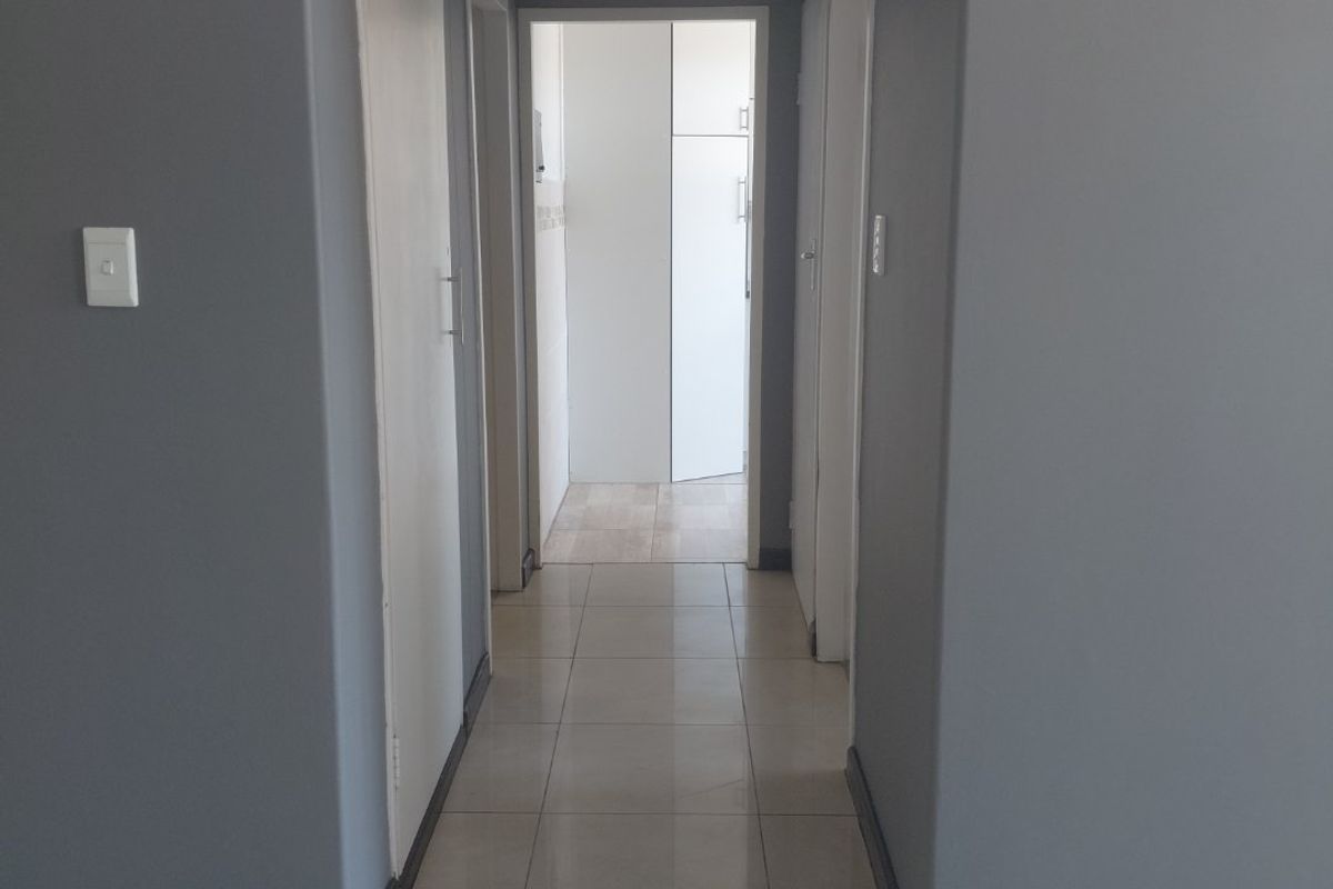 A clean, neutral-toned hallway featuring tiled flooring, built-in storage cupboards, and direct access to adjacent rooms.