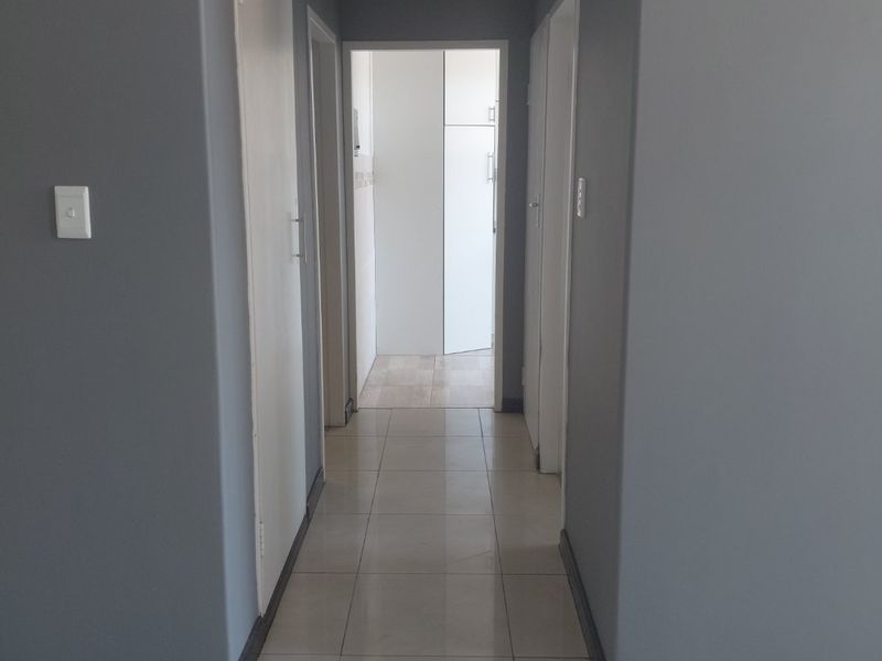 A clean, neutral-toned hallway featuring tiled flooring, built-in storage cupboards, and direct access to adjacent rooms.