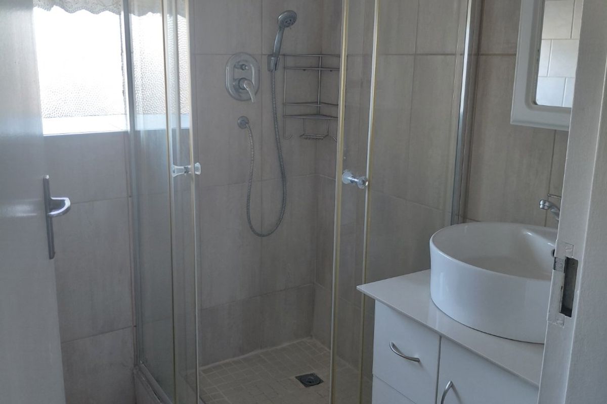 A compact bathroom featuring a glass-enclosed shower, a modern vessel sink set on a white vanity cabinet, and neutral wall and floor tiling.
