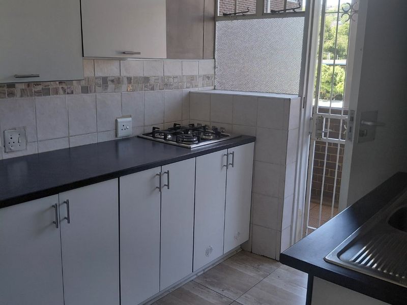 A functional kitchen featuring white cabinetry, dark countertops, a gas hob, and tiled flooring with direct access to an exterior balcony.