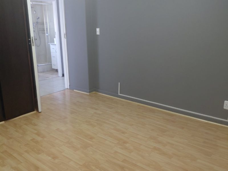 A vacant bedroom featuring light laminate flooring, grey painted walls, a built-in cupboard, and direct access to an en-suite bathroom.
