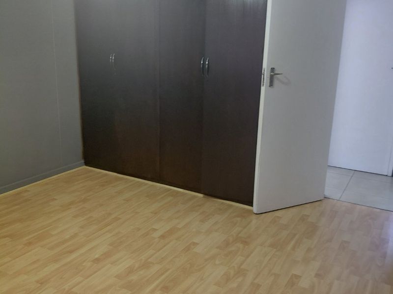 An empty bedroom featuring dark built-in cupboards, light-toned laminate flooring, and neutral grey walls.