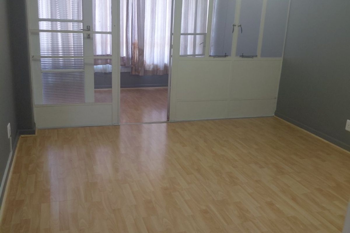An empty bedroom featuring light-toned laminate flooring and a glass partition wall leading to an adjacent space.