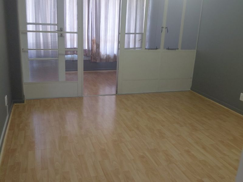 An empty bedroom featuring light-toned laminate flooring and a glass partition wall leading to an adjacent space.