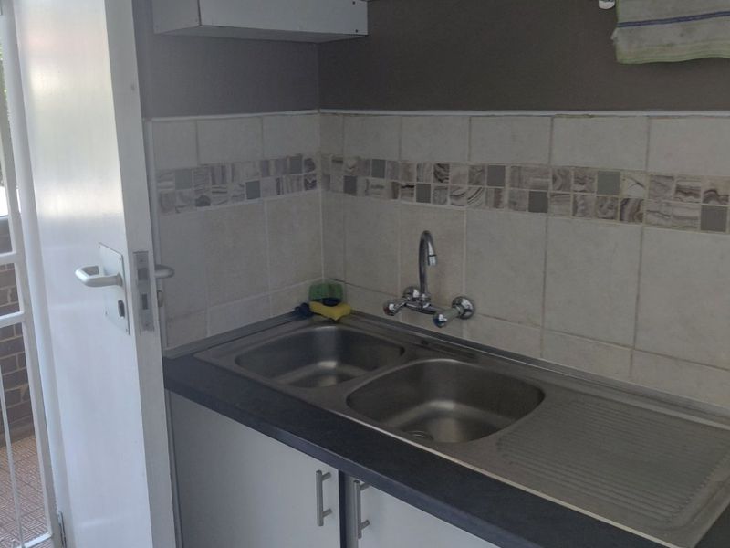 A compact scullery area featuring a stainless steel double sink, laminate countertop, and tiled splashback with built-in cabinetry.