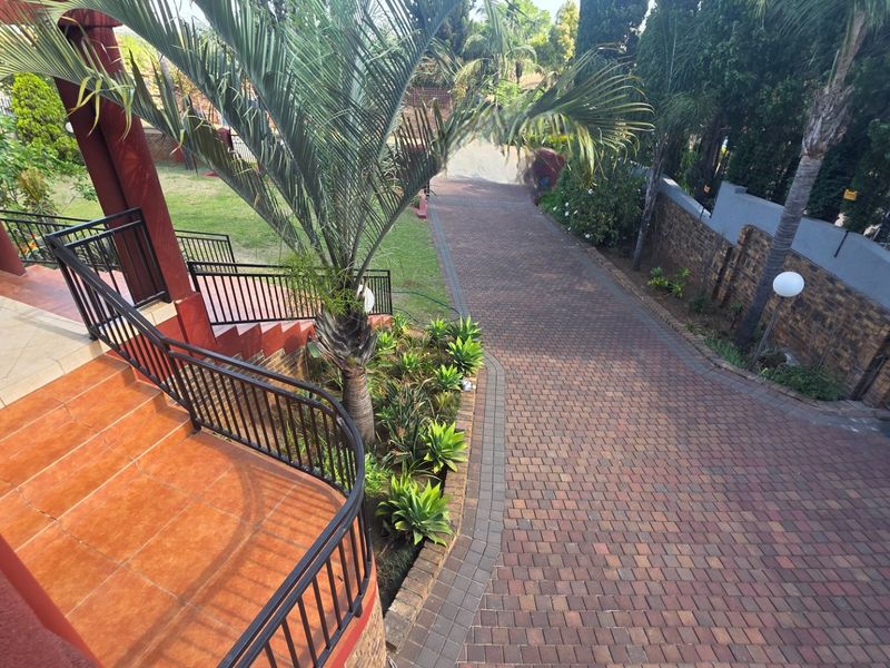 A view of the property entrance featuring a paved driveway, tiled patio with metal railings, and a well-maintained garden area.