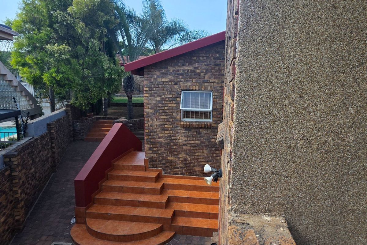 Rear exterior view of the property featuring a face brick facade, tiled staircase, and paved courtyard area.